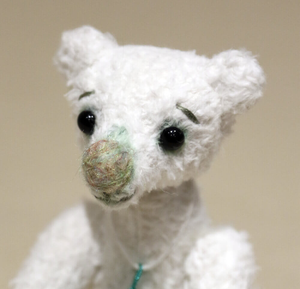 Pistachio - handmade artist bear by Brierley Bears. White viscose with green detailing, black glass eyes and large needle felted nose. Close up of face.