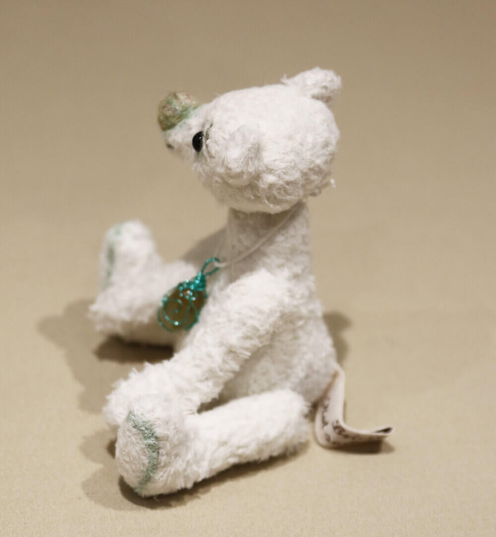 Pistachio is a little white viscose bear with green detailing. Handmade by Brierley Bears. Photo shows bears left side, sitting.