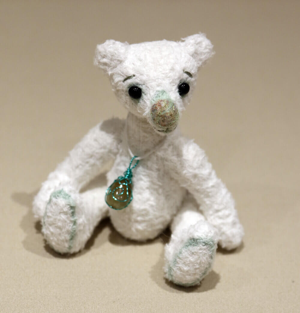 Pistachio - handmade white artisan bear. Made from white viscose with green detailing. Sitting, looking left. Big needle felted nose and black glass eyes. Wears a crystal pendant.